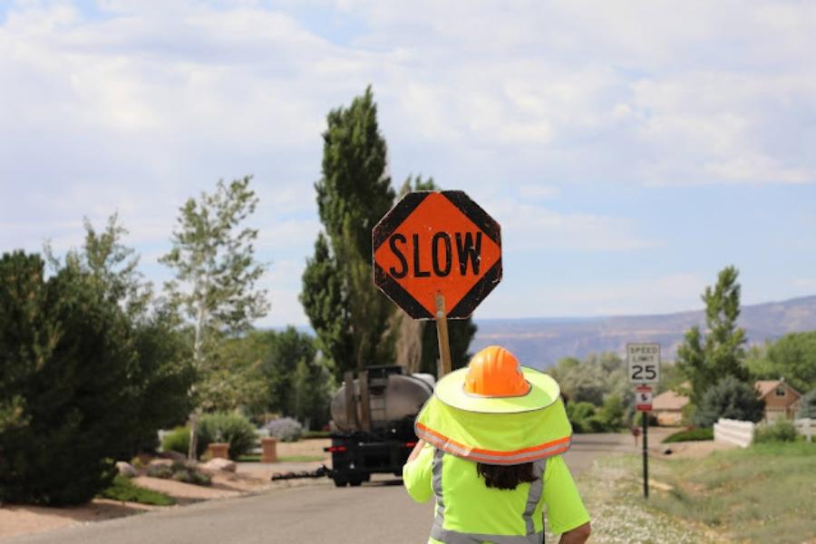 Construction worker holds orange SLOW sign in bright yellow vest. 