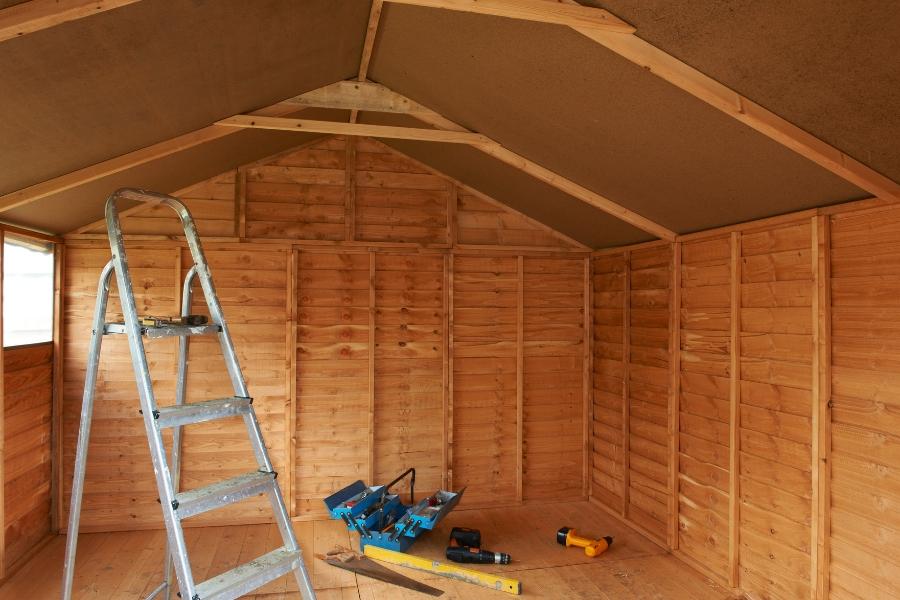 Inside view of wooden shed with ladder and tools inside. 