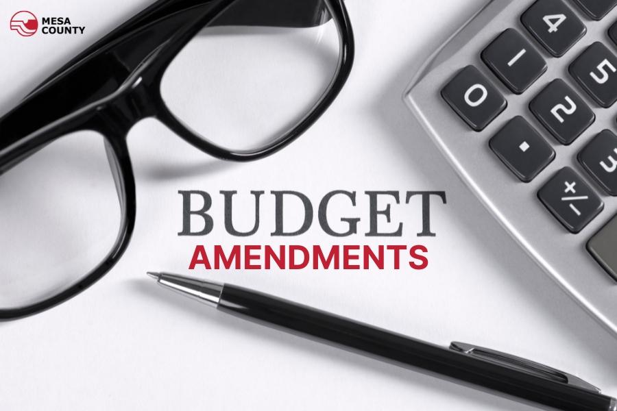Glasses, a pen, and a calculator with black and red text reading, BUDGET AMENDMENTS.