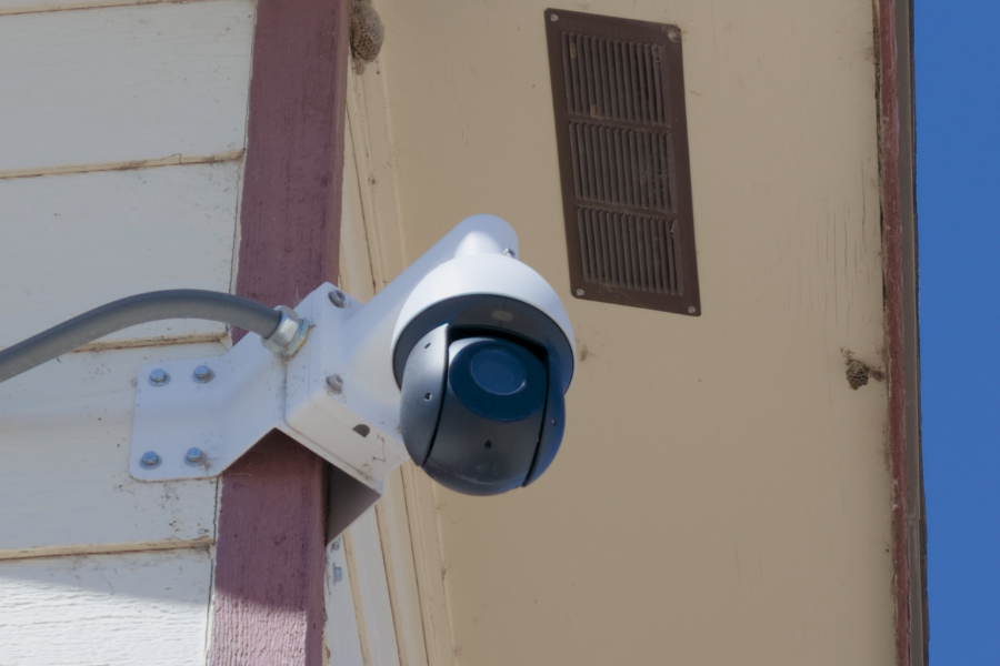 Close up photo of an automated license plate reader camera mounted high on the corner of a building in Mesa County, with blue sky in the background.